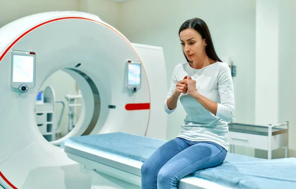 An agitated, sad and frightened patient sits on the bed of a CT or MRI machine. In a medical laboratory with high-tech equipment.