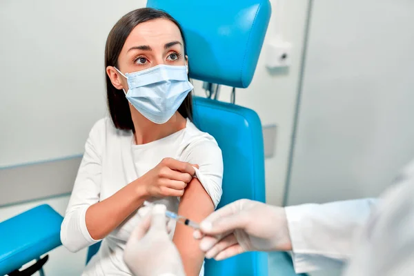 Vaccination, immunization campaign, disease prevention concept. Young woman in medical face mask getting Covid-19 vaccine at doctor\'s office. Professional nurse giving flu injection to patient