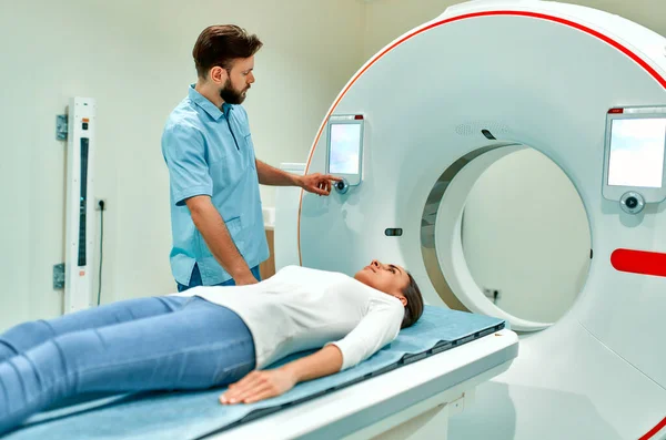 The patient lies on CT or MRI, the bed is moved inside the machine, scanning her body and brain under the supervision of a doctor. In a medical laboratory with high-tech equipment.