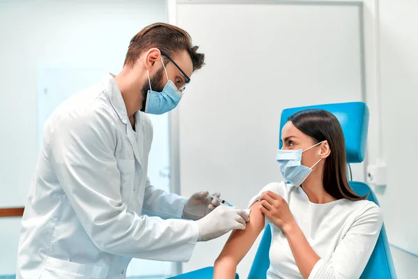 Vaccination, immunization campaign, disease prevention concept. Young woman in medical face mask getting Covid-19 vaccine at doctor\'s office. Professional nurse giving flu injection to patient