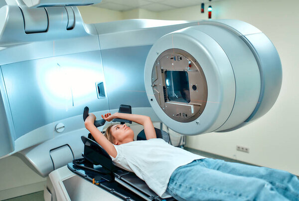 A young woman is undergoing radiation therapy for cancer in a modern cancer hospital. Cancer treatment, modern medical linear accelerator.