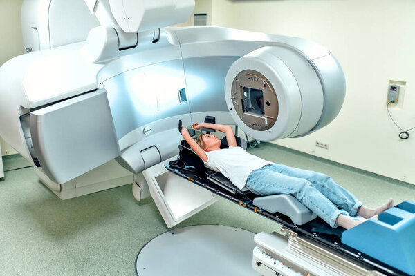 A young woman is undergoing radiation therapy for cancer in a modern cancer hospital. Cancer treatment, modern medical linear accelerator.