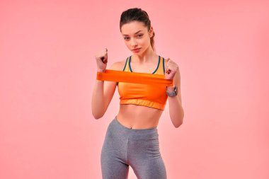 Spor giyim kuşağında spor lastiğiyle egzersiz yapan sevimli bir kız pembe arka planda izole edilmiş. Spor, yoga, aktif yaşam tarzı, sağlık için egzersiz.