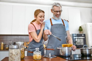 Önlüklü mutlu çift mutfakta makarna hazırlıyor ve iyi vakit geçiriyorlar. Vejetaryen, vejetaryen, sağlıklı yaşam tarzı.