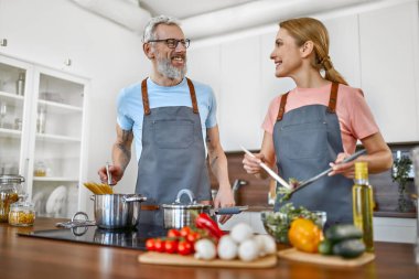 Önlüklü mutlu çift mutfakta makarna ve taze salata hazırlıyor ve iyi vakit geçiriyorlar. Vejetaryen, vejetaryen, sağlıklı yaşam tarzı.