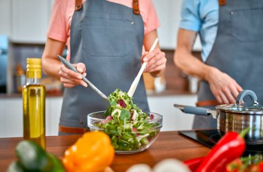Önlüklü mutlu çift mutfakta makarna ve taze salata hazırlıyor ve iyi vakit geçiriyorlar. Vejetaryen, vejetaryen, sağlıklı yaşam tarzı.