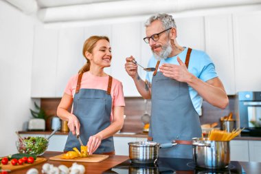 Önlüklü mutlu çift mutfakta makarna ve taze salata hazırlıyor ve iyi vakit geçiriyorlar. Vejetaryen, vejetaryen, sağlıklı yaşam tarzı.