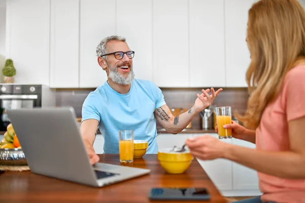 Happy married couple have breakfast and have fun using laptop in the kitchen. Healthy lifestyle concept.