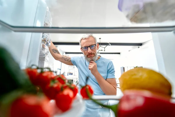 成熟した男は何かを調理または食べるために冷蔵庫を開いた 冷蔵庫からの眺め 健康食品のコンセプト — ストック写真
