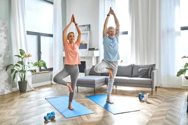 Sport, fitness and healthy lifestyle concept. Mature couple doing exercise or yoga at home. How to stay healthy in quarantine.