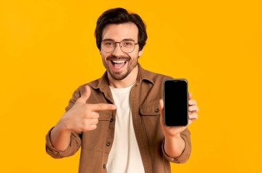 Gözlüklü genç sakallı adam turuncu arka planda boş bir akıllı telefon ekranında görünüyor..