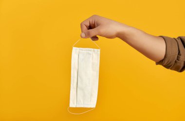 Turuncu arka planda koruyucu bir tıbbi maske tutan bir erkek. COVID-19 koronavirüs enfeksiyonu karantinasında yaşam.