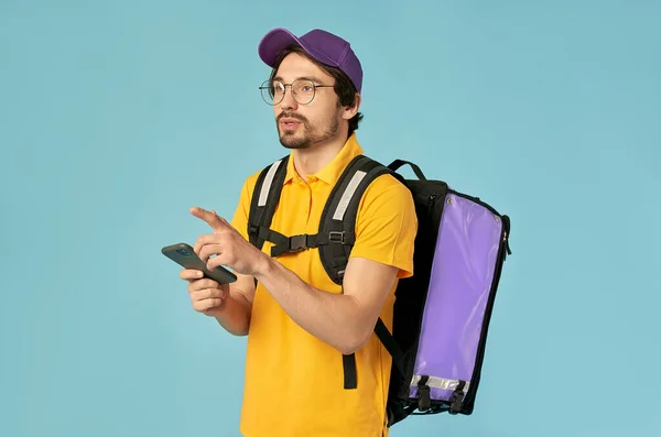 一个年轻信使的画像 穿着制服的送货人 带着热身背包和一个蓝色背景的智能手机 快送货上门网上订购 — 图库照片