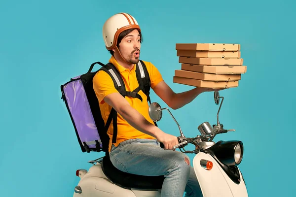 Young courier, pizza delivery man in uniform with thermo backpack on a moped isolated on blue background. Fast transport express home delivery. Online order.