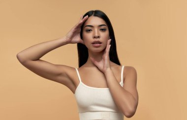 Beyaz bluzlu, temiz, parlak derili genç Asyalı kadın bej arka planda izole edilmiş. Yüz bakımı konsepti, spa, kozmetoloji, estetik cerrahi.