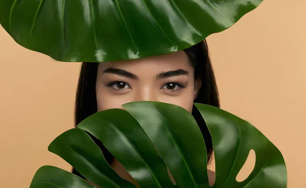 ベージュ地に緑の葉を持つきれいな放射状の顔の皮膚を持つ若いアジアの女性 スパケア 顔のスキンケア 美容美容 天然化粧品のコンセプト — ストック写真