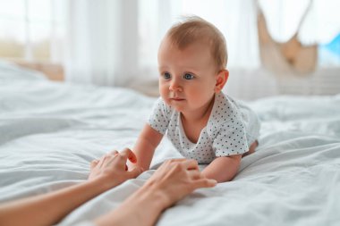 Sevgi dolu anne, yeni doğmuş bebeğini evde taşıyor. Anne ve çocuğu beyaz bir yatakta. Anne ve bebek bezi giymiş çocuk güneşli yatak odasında oynuyorlar. Ebeveyn ve küçük çocuk evde dinleniyor. Aile birlikte eğleniyor..