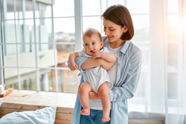 Sevgi dolu bir anne, yeni doğmuş bebeğini evde taşıyor. Anne ve oğlu güneşli yatak odasında oynuyorlar. Ebeveyn ve küçük çocuk evde dinleniyor. Aile birlikte eğleniyor. Çocuk bakımı, annelik kavramı.