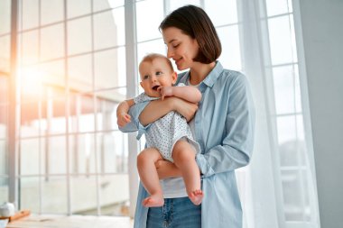 Sevgi dolu bir anne, yeni doğmuş bebeğini evde taşıyor. Anne ve oğlu güneşli yatak odasında oynuyorlar. Ebeveyn ve küçük çocuk evde dinleniyor. Aile birlikte eğleniyor. Çocuk bakımı, annelik kavramı.