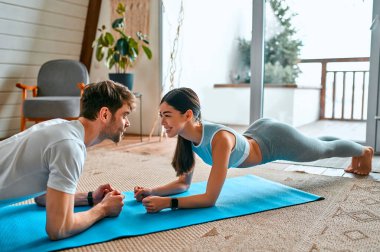 Spor giyimli şirin bir çift evdeki oturma odasındaki paspasların üzerinde egzersiz tahtası yapıyor. Sağlıklı yaşam tarzı, spor, yoga, spor.