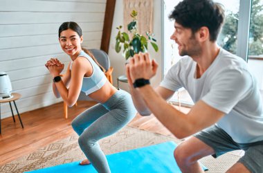 Şirin Koreli kadın ve spor elbiseli kaslı adam evdeki oturma odasındaki paspaslara çömelmiş egzersiz yapıyorlar. Sağlıklı yaşam tarzı, yoga, spor, spor.