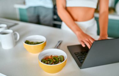 Genç bir çift mutfakta kahvaltı yapıyor. Sağlıklı yemek, kilo kaybı. Beyaz iç çamaşırlı bir kız laptop kullanıyor..