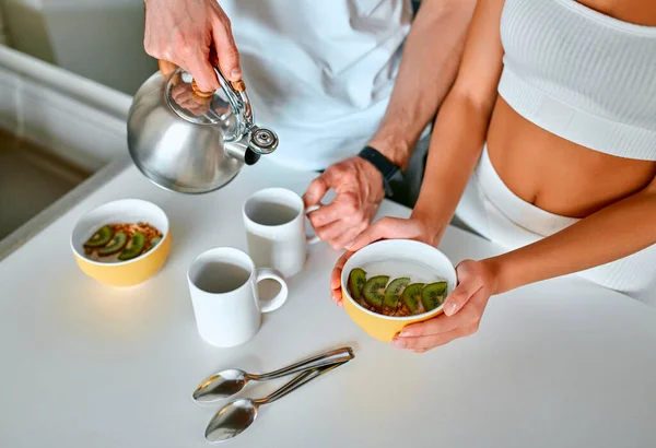 A young couple in the kitchen have breakfast and drink tea in the morning. Healthy sports nutrition, weight loss.