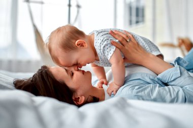 Sevgi dolu bir anne, yeni doğmuş bebeğini evde taşıyor. Anne ve oğlu güneşli yatak odasında oynuyorlar. Ebeveyn ve küçük çocuk evde dinleniyor. Aile birlikte eğleniyor. Çocuk bakımı, annelik kavramı.