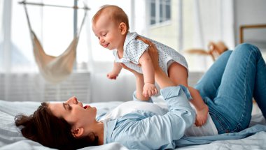 Sevgi dolu bir anne, yeni doğmuş bebeğini evde taşıyor. Anne ve oğlu güneşli yatak odasında oynuyorlar. Ebeveyn ve küçük çocuk evde dinleniyor. Aile birlikte eğleniyor. Çocuk bakımı, annelik kavramı.