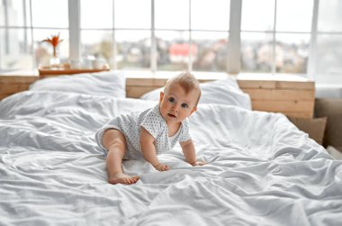 Beyaz güneşli yatak odasında sevimli bir erkek bebek. Yeni doğmuş çocuk yatakta dinleniyor. Küçük çocuklar için çocuk odası. Çocuklar için tekstil ve yatak. Aile sabahı evde. Karnında yeni doğan çocuk..