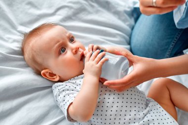 Annesine bakarken biberondan süt içen tatlı bir bebek. Anne oğlunu biberondan besliyor. Küçük çocuk evde süt içiyor..