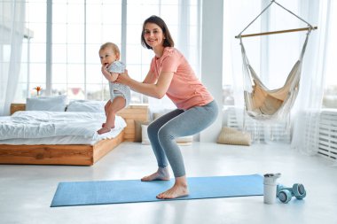 Sporcu bir anne evde yoga ve spor salonunda çocukla meşgul olur. Spor konsepti, annelik ve aktif yaşam tarzı. Çocuğuyla spor eğitimi alan genç bir kadın..