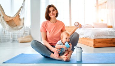 Sporcu bir anne evde yoga ve spor salonunda çocukla meşgul olur. Spor konsepti, annelik ve aktif yaşam tarzı. Çocuğuyla spor eğitimi alan genç bir kadın..