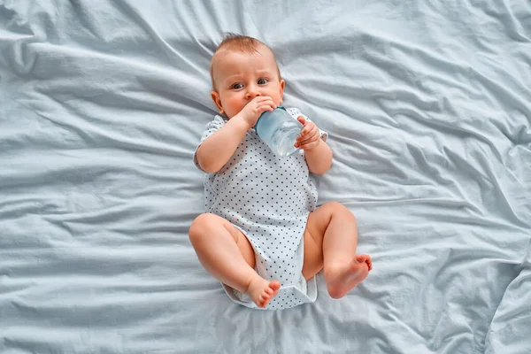 Cute Little Boy Pije Wodę Butelki Leżąc Łóżku Domu — Zdjęcie stockowe