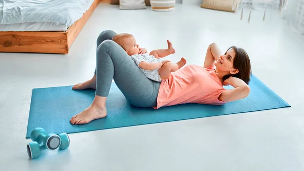一位运动母亲在家里和孩子一起练健身和瑜伽 母性和积极的生活方式的概念 与孩子一起参加体育培训的年轻妇女 — 图库照片