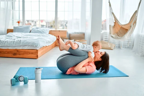 一位运动母亲在家里和孩子一起练健身和瑜伽 母性和积极的生活方式的概念 与孩子一起参加体育培训的年轻妇女 — 图库照片