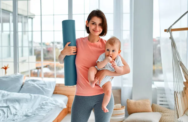 A sports mother is engaged with the child in fitness and yoga at home. The concept of sports, motherhood and an active lifestyle. Young woman in sports training with her child.