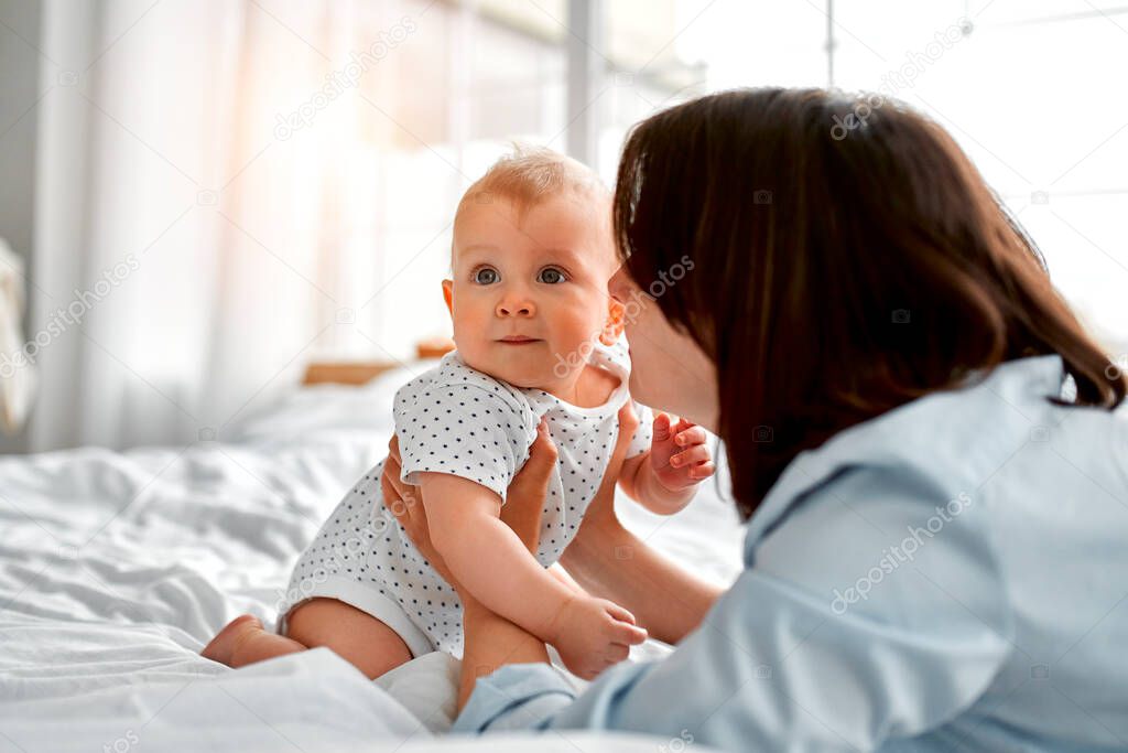 Loving mom carying of her newborn baby at home.Mom and baby boy playing in sunny bedroom. Parent and little kid relaxing at home. Family having fun together. Childcare, maternity concept.