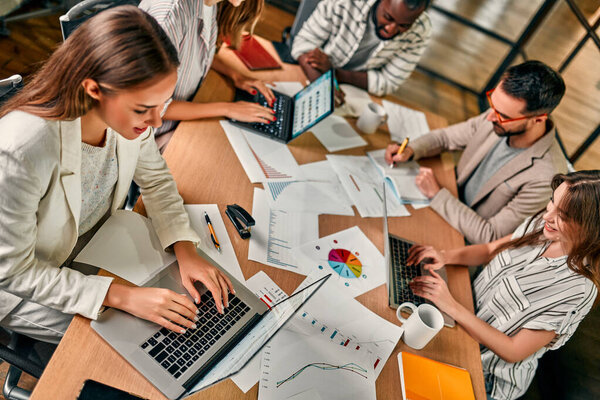 Multiracial young creative people in a modern office. A group of young business people are working together with a laptop, smartphone. A successful hipster team in a coworking space.