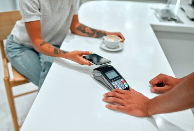 Bayan müşteri, kafede cep telefonuyla genç bir adamla ödeme yapıyor. Barista 'nın elinde cep telefonu olan kadın kostümcünün önünde kredi kartı okuma makinesi var..