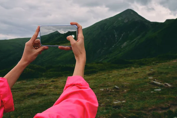 山の草で覆われた女性のハイカー 霧と曇りの天気の山の風景です 女性の手はスマートフォンで写真を撮る — ストック写真