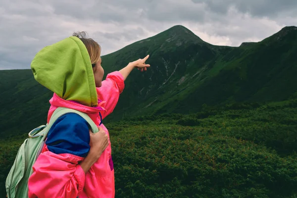 山の草で覆われた女性のハイカー 霧と曇りの天気の山の風景です 観光客は彼の指を山の頂上に向けます — ストック写真
