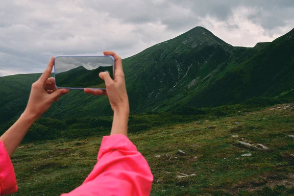 山の草で覆われた女性のハイカー 霧と曇りの天気の山の風景です 女性の手はスマートフォンで写真を撮る — ストック写真