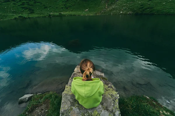 女性の観光客は山のふもとの湖の近くの石の上に座っている レクリエーション — ストック写真