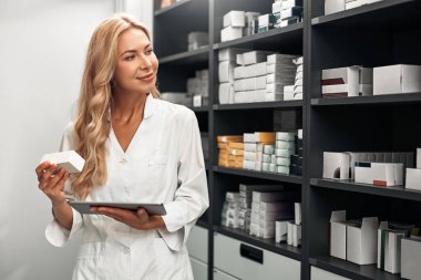 Gülümseyen kadın eczacı eczane deposunda ilaç stokunu kontrol ediyor. Konsept: eczane işi.