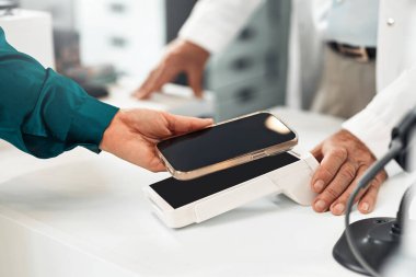 Akıllı telefonuyla ödeme yapan bir kadının eczane tezgahındaki bağlantısız ödemesini çekiyoruz. Kavram: dijital işlem, modern sağlık hizmeti, mobil teknoloji.