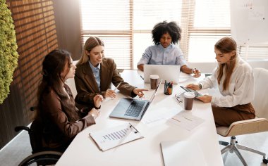 Ofiste birlikte çalışan çeşitli genç profesyonellerden oluşan bir ekip. Tekerlekli sandalyedeki kadın tartışmaya katılıyor. Katılım ve takım çalışması kavramı.