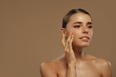 Kafkasyalı kadın gözleri kapalı gülümsüyor, nazikçe yüzüne dokunuyor. Doğal makyaj ve parlayan cilt. Cilt bakımı, neşe ve kendini beğenme temaları için mükemmel. Konsept: Güven ve güzellik