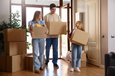 Taşınırken karton kutuları olan üç kişilik neşeli bir aile. Parlak iç mekan, takım çalışması ve neşeli ifadeler. Taşınma kavramı, yeni bir başlangıç ve aile desteği.