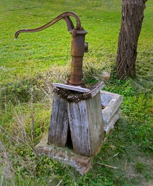 オーストリアの牧草地にある腐った木のベースに古い錆びた手ポンプ — ストック写真